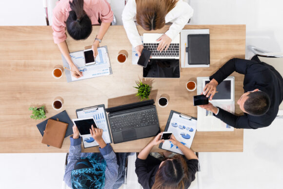 Top view of businessman executive in group meeting with other businessmen and businesswomen in modern office with laptop computer, coffee and document on table. People corporate business team concept.